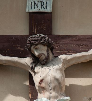 Zdjęcie nr 5: Grupa rzeźbiarska umieszczona we wnęce w formie stojącego prostokąta zamkniętego łukiem półkolistym. W centrum krzyż wypełniający całą wnękę, osadzony na skale, do którego trzema gwoździami przybita jest figura umarłego Chrystusa. Ciało ma w lekkim zwisie, o horyzontalnie rozłożonych ramionach, jego głowa opada na prawy bark, nogi ma lekko ugięte w kolanach, a stopy skrzyżowane w układzie prawa na lewą. Twarz ma szczupłą, o zamkniętych oczach, dużym nosie i otwartych ustach, okoloną krótką, kręconą brodą oraz falowanymi, brązowymi włosami, opadającymi na prawe ramię. Na głowie ma szeroką, brązową koronę cierniową. Ciało o lekko podkreślonej muskulaturze i silnie zaznaczonych żebrach klatki piersiowej. Przez biodra przewiązane krótkie, białe perizonium ze zwisem tkaniny na prawym boku. 
Po lewej stronie krzyża figura Marii, ustawiona na półkolistej podstawie. Matka Boska zwrócona w trzech czwartych w lewo, z pochyloną głową oraz rękami skrzyżowanymi na piersi. Twarz ma owalną, o dużych, migdałowatych oczach, dużym nosie i wąskich ustach. Ubrana jest w białą suknię oraz jasnoniebieski płaszcz z szerokimi rękawami, rozchylony z przodu, na głowę ma narzucony biały welon opadający na ramiona. 
Po prawej stronie krzyża figura św. Jana ustawiona na półkolistej podstawie. Święty zwrócony w trzech czwartych w prawo, w kontrapoście, z uniesionymi, splecionymi dłońmi. Twarz ma szczupłą, o migdałowatych oczach, prostym nosie i wąskich ustach, okoloną gęstymi, kręconymi, brązowymi włosami, opadającymi na ramiona. Ubrany jest w jasnoniebieską suknię oraz zawiązany diagonalnie przez prawe ramię czerwony płaszcz. Polichromia ciał naturalistyczna. 
