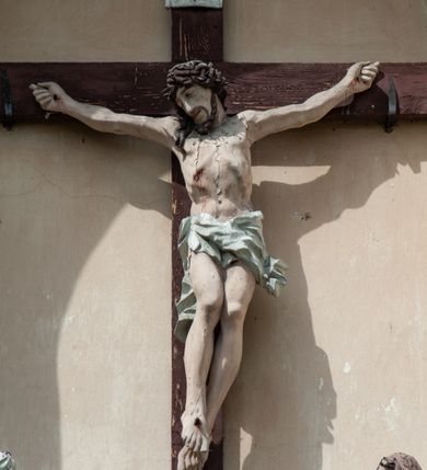 Zdjęcie nr 2: Grupa rzeźbiarska umieszczona we wnęce w formie stojącego prostokąta zamkniętego łukiem półkolistym. W centrum krzyż wypełniający całą wnękę, osadzony na skale, do którego trzema gwoździami przybita jest figura umarłego Chrystusa. Ciało ma w lekkim zwisie, o horyzontalnie rozłożonych ramionach, jego głowa opada na prawy bark, nogi ma lekko ugięte w kolanach, a stopy skrzyżowane w układzie prawa na lewą. Twarz ma szczupłą, o zamkniętych oczach, dużym nosie i otwartych ustach, okoloną krótką, kręconą brodą oraz falowanymi, brązowymi włosami, opadającymi na prawe ramię. Na głowie ma szeroką, brązową koronę cierniową. Ciało o lekko podkreślonej muskulaturze i silnie zaznaczonych żebrach klatki piersiowej. Przez biodra przewiązane krótkie, białe perizonium ze zwisem tkaniny na prawym boku. 
Po lewej stronie krzyża figura Marii, ustawiona na półkolistej podstawie. Matka Boska zwrócona w trzech czwartych w lewo, z pochyloną głową oraz rękami skrzyżowanymi na piersi. Twarz ma owalną, o dużych, migdałowatych oczach, dużym nosie i wąskich ustach. Ubrana jest w białą suknię oraz jasnoniebieski płaszcz z szerokimi rękawami, rozchylony z przodu, na głowę ma narzucony biały welon opadający na ramiona. 
Po prawej stronie krzyża figura św. Jana ustawiona na półkolistej podstawie. Święty zwrócony w trzech czwartych w prawo, w kontrapoście, z uniesionymi, splecionymi dłońmi. Twarz ma szczupłą, o migdałowatych oczach, prostym nosie i wąskich ustach, okoloną gęstymi, kręconymi, brązowymi włosami, opadającymi na ramiona. Ubrany jest w jasnoniebieską suknię oraz zawiązany diagonalnie przez prawe ramię czerwony płaszcz. Polichromia ciał naturalistyczna. 
