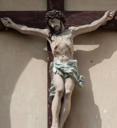 Zdjęcie nr 3: Grupa rzeźbiarska umieszczona we wnęce w formie stojącego prostokąta zamkniętego łukiem półkolistym. W centrum krzyż wypełniający całą wnękę, osadzony na skale, do którego trzema gwoździami przybita jest figura umarłego Chrystusa. Ciało ma w lekkim zwisie, o horyzontalnie rozłożonych ramionach, jego głowa opada na prawy bark, nogi ma lekko ugięte w kolanach, a stopy skrzyżowane w układzie prawa na lewą. Twarz ma szczupłą, o zamkniętych oczach, dużym nosie i otwartych ustach, okoloną krótką, kręconą brodą oraz falowanymi, brązowymi włosami, opadającymi na prawe ramię. Na głowie ma szeroką, brązową koronę cierniową. Ciało o lekko podkreślonej muskulaturze i silnie zaznaczonych żebrach klatki piersiowej. Przez biodra przewiązane krótkie, białe perizonium ze zwisem tkaniny na prawym boku. 
Po lewej stronie krzyża figura Marii, ustawiona na półkolistej podstawie. Matka Boska zwrócona w trzech czwartych w lewo, z pochyloną głową oraz rękami skrzyżowanymi na piersi. Twarz ma owalną, o dużych, migdałowatych oczach, dużym nosie i wąskich ustach. Ubrana jest w białą suknię oraz jasnoniebieski płaszcz z szerokimi rękawami, rozchylony z przodu, na głowę ma narzucony biały welon opadający na ramiona. 
Po prawej stronie krzyża figura św. Jana ustawiona na półkolistej podstawie. Święty zwrócony w trzech czwartych w prawo, w kontrapoście, z uniesionymi, splecionymi dłońmi. Twarz ma szczupłą, o migdałowatych oczach, prostym nosie i wąskich ustach, okoloną gęstymi, kręconymi, brązowymi włosami, opadającymi na ramiona. Ubrany jest w jasnoniebieską suknię oraz zawiązany diagonalnie przez prawe ramię czerwony płaszcz. Polichromia ciał naturalistyczna. 
