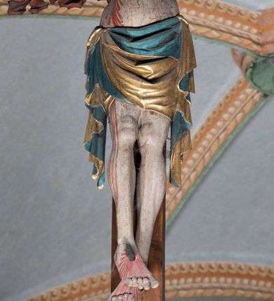 Zdjęcie nr 2: Rzeźba pełnoplastyczna, z tyłu opracowana. Ciało Chrystusa przybite do krzyża na niemal horyzontalnie, szeroko rozłożonych ramionach. Głowa w koronie cierniowej pochylona na prawe ramię. Długie włosy w puklach o spiralnie zakończonych lokach opadają na ramiona i plecy. Twarz szczupła o zindywidualizowanych rysach, pełna spokoju i smutku, okolona krótkim zarostem, z wydatnymi kośćmi policzkowymi, z kroplami krwi na czole. Duże, okrągłe oczy przesłonięte powiekami, podkreślone uniesionymi łukami brwiowymi. Usta drobne, zaciśnięte, nos prosty, wąski. Ręce chude długie, silnie wyprężone, dłonie rozchylone, przebite gwoździami. Klatka piersiowa o starannie opracowanej anatomii, z silnym wcięciem w talii oraz raną w prawym boku. Perizonium w kształcie chusty, sięgające do połowy uda, miękko udrapowane z przodu, spływające po obu bokach kaskadowymi fałdami. Nogi wyprostowane, umięśnione, ułożone obok siebie, stopy stosunkowo duże, skrzyżowane, założone prawa na lewą, przebite jednym gwoździem. Z ran na boku, dłoniach i stopach spływa obficie krew. Karnacja Chrystusa jasnoróżowa, włosy brązowe z domalowanym warkoczem z tyłu, korona zielona, perizonium złocone, z niebieską podszewką. Krzyż łaciński, dębowy, w naturalnym kolorze drewna, wykonany w 1890, w formie Drzewa Życia, z rozłożystymi liśćmi uschniętego akantu w kolorze czerwonym i złotym żyłkowaniem na skrzyżowaniu ramion. W zakończeniu ramion lilijki czerwono-zielone ze złoconymi obwódkami oraz nakładane plakiety w układzie koncentrycznym tworzące ośmioramienne gwiazdy z płaskorzeźbionymi symbolami Ewangelistów. Tła plakiet malowane na niebiesko, symbole i obramienia złocone. Plakiety współczesne z rzeźbą Chrystusa, gotyckie - 1433 r.; u góry krzyża - symbol św. Jana - orzeł, u dołu - symbol św. Łukasza - wół, na prawym ramieniu symbol św. Mateusza - anioł, na lewym ramieniu - symbol św. Marka - lew. Ponad głową Chrystusa titulus z napisem: INRI. Plakieta kwadratowa nałożona na romb w układzie koncentrycznym, w profilowanym obramieniu, z płaskorzeźbionym przedstawieniem orła; u dołu banderola z napisem minuskułą gotycką: sanctus joannes. Plakieta kwadratowa nałożona na romb w układzie koncentrycznym, w obramieniu profilowanym, z fazą wklęsłą - z płaskorzeźbionym przedstawieniem anioła w pozycji siedzącej z podkurczonymi nogami w ujęciu frontalnym, w rękach podtrzymującego faliście wygiętą banderolę o zrolowanych zakończeniach, z czarnym napisem minuskułą gotycką: sanctus matheus; banderola biała z czarnymi rozetkami. Twarz anioła okrągła, o rysach dziecka, różowa, okolona puklami rudych włosów. Anioł ubrany w fałdzistą szatę, złoconą z trójkątnym dekoltem, udrapowaną na kolanach w głębokie, łyżkowate fałdy. U ramion szeroko rozpostarte skrzydła o schematycznych rombowych podziałach, zagięte na brzegach, zakończone długimi piórami, lotkami - złocone. Tło lekko pogłębione, niebieskie; obramienia kwadratów złocone, boki i tylne ściany malowane na brązowo. Plakieta kwadratowa nałożona na romb w układzie koncentrycznym, w obramieniu profilowanym, z fazą wklęsłą, z płaskorzeźbionym przedstawieniem uskrzydlonego wołu, w pełnej postaci, w ujęciu bocznym, o masywnej budowie ciała, w dynamicznym ruchu, wspartego na rozstawionych nogach, zakończonych ciężkimi kopytami, z puszystym ogonem. Głowa zwrócona na wprost, oczy duże, nozdrza rozdęte, uszy odstające na boki, pośrodku ozdobnie osadzone esowato wygięte rogi. Skrzydła wyrastające z barków, uniesione w górę, rozpostarte, upierzenie schematyczne zaznaczone w kształcie rombów, z długimi lotkami w zakończeniach wygiętych skrzydeł. U dołu, pomiędzy nogami zwierzęcia - półkoliście wygięta biała banderola, z czarnym napisem minuskułą gotycką: sanctus lucas i czarnymi rozetkami. Tło nieco pogłębione, niebieskie. Postać wołu, obramienie plakiet, złocone; ścianki tylne malowane na brązowo. Plakieta w kształcie rombu nałożonego na kwadrat w układzie koncentrycznym, w obramieniu profilowanym, z fazą wklęsłą - z płaskorzeźbionym przedstawieniem uskrzydlonego lwa. W pełnej postaci, ujęciu bocznym, muskularnych kształtach, mocnych nogach z potężnymi pazurami. Głowa zwrócona na wprost, ujęta bujną, silnie skręconą grzywą. Skrzydła wyrastające z barków uniesione w górę, szeroko rozpostarte, zakończone długimi lotkami; upierzenie schematycznie zaznaczone w formie regularnych rombów. Ogon cienki, długi, z puszystą kitką, przechodzący pomiędzy nogami, esowato wygięty nad grzbietem. U dołu biała banderola, podtrzymywana pazurami przednich łap, z napisem czarnym, gotycką minuskułą: sanctus marcus i czarnymi rozetkami. Tło nieco pogłębione, niebieskie; postać lwa i obramienia złocone, tylne ścianki malowane na brązowo.