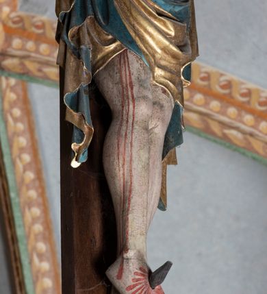 Zdjęcie nr 13: Rzeźba pełnoplastyczna, z tyłu opracowana. Ciało Chrystusa przybite do krzyża na niemal horyzontalnie, szeroko rozłożonych ramionach. Głowa w koronie cierniowej pochylona na prawe ramię. Długie włosy w puklach o spiralnie zakończonych lokach opadają na ramiona i plecy. Twarz szczupła o zindywidualizowanych rysach, pełna spokoju i smutku, okolona krótkim zarostem, z wydatnymi kośćmi policzkowymi, z kroplami krwi na czole. Duże, okrągłe oczy przesłonięte powiekami, podkreślone uniesionymi łukami brwiowymi. Usta drobne, zaciśnięte, nos prosty, wąski. Ręce chude długie, silnie wyprężone, dłonie rozchylone, przebite gwoździami. Klatka piersiowa o starannie opracowanej anatomii, z silnym wcięciem w talii oraz raną w prawym boku. Perizonium w kształcie chusty, sięgające do połowy uda, miękko udrapowane z przodu, spływające po obu bokach kaskadowymi fałdami. Nogi wyprostowane, umięśnione, ułożone obok siebie, stopy stosunkowo duże, skrzyżowane, założone prawa na lewą, przebite jednym gwoździem. Z ran na boku, dłoniach i stopach spływa obficie krew. Karnacja Chrystusa jasnoróżowa, włosy brązowe z domalowanym warkoczem z tyłu, korona zielona, perizonium złocone, z niebieską podszewką. Krzyż łaciński, dębowy, w naturalnym kolorze drewna, wykonany w 1890, w formie Drzewa Życia, z rozłożystymi liśćmi uschniętego akantu w kolorze czerwonym i złotym żyłkowaniem na skrzyżowaniu ramion. W zakończeniu ramion lilijki czerwono-zielone ze złoconymi obwódkami oraz nakładane plakiety w układzie koncentrycznym tworzące ośmioramienne gwiazdy z płaskorzeźbionymi symbolami Ewangelistów. Tła plakiet malowane na niebiesko, symbole i obramienia złocone. Plakiety współczesne z rzeźbą Chrystusa, gotyckie - 1433 r.; u góry krzyża - symbol św. Jana - orzeł, u dołu - symbol św. Łukasza - wół, na prawym ramieniu symbol św. Mateusza - anioł, na lewym ramieniu - symbol św. Marka - lew. Ponad głową Chrystusa titulus z napisem: INRI. Plakieta kwadratowa nałożona na romb w układzie koncentrycznym, w profilowanym obramieniu, z płaskorzeźbionym przedstawieniem orła; u dołu banderola z napisem minuskułą gotycką: sanctus joannes. Plakieta kwadratowa nałożona na romb w układzie koncentrycznym, w obramieniu profilowanym, z fazą wklęsłą - z płaskorzeźbionym przedstawieniem anioła w pozycji siedzącej z podkurczonymi nogami w ujęciu frontalnym, w rękach podtrzymującego faliście wygiętą banderolę o zrolowanych zakończeniach, z czarnym napisem minuskułą gotycką: sanctus matheus; banderola biała z czarnymi rozetkami. Twarz anioła okrągła, o rysach dziecka, różowa, okolona puklami rudych włosów. Anioł ubrany w fałdzistą szatę, złoconą z trójkątnym dekoltem, udrapowaną na kolanach w głębokie, łyżkowate fałdy. U ramion szeroko rozpostarte skrzydła o schematycznych rombowych podziałach, zagięte na brzegach, zakończone długimi piórami, lotkami - złocone. Tło lekko pogłębione, niebieskie; obramienia kwadratów złocone, boki i tylne ściany malowane na brązowo. Plakieta kwadratowa nałożona na romb w układzie koncentrycznym, w obramieniu profilowanym, z fazą wklęsłą, z płaskorzeźbionym przedstawieniem uskrzydlonego wołu, w pełnej postaci, w ujęciu bocznym, o masywnej budowie ciała, w dynamicznym ruchu, wspartego na rozstawionych nogach, zakończonych ciężkimi kopytami, z puszystym ogonem. Głowa zwrócona na wprost, oczy duże, nozdrza rozdęte, uszy odstające na boki, pośrodku ozdobnie osadzone esowato wygięte rogi. Skrzydła wyrastające z barków, uniesione w górę, rozpostarte, upierzenie schematyczne zaznaczone w kształcie rombów, z długimi lotkami w zakończeniach wygiętych skrzydeł. U dołu, pomiędzy nogami zwierzęcia - półkoliście wygięta biała banderola, z czarnym napisem minuskułą gotycką: sanctus lucas i czarnymi rozetkami. Tło nieco pogłębione, niebieskie. Postać wołu, obramienie plakiet, złocone; ścianki tylne malowane na brązowo. Plakieta w kształcie rombu nałożonego na kwadrat w układzie koncentrycznym, w obramieniu profilowanym, z fazą wklęsłą - z płaskorzeźbionym przedstawieniem uskrzydlonego lwa. W pełnej postaci, ujęciu bocznym, muskularnych kształtach, mocnych nogach z potężnymi pazurami. Głowa zwrócona na wprost, ujęta bujną, silnie skręconą grzywą. Skrzydła wyrastające z barków uniesione w górę, szeroko rozpostarte, zakończone długimi lotkami; upierzenie schematycznie zaznaczone w formie regularnych rombów. Ogon cienki, długi, z puszystą kitką, przechodzący pomiędzy nogami, esowato wygięty nad grzbietem. U dołu biała banderola, podtrzymywana pazurami przednich łap, z napisem czarnym, gotycką minuskułą: sanctus marcus i czarnymi rozetkami. Tło nieco pogłębione, niebieskie; postać lwa i obramienia złocone, tylne ścianki malowane na brązowo.