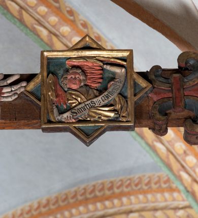 Zdjęcie nr 7: Rzeźba pełnoplastyczna, z tyłu opracowana. Ciało Chrystusa przybite do krzyża na niemal horyzontalnie, szeroko rozłożonych ramionach. Głowa w koronie cierniowej pochylona na prawe ramię. Długie włosy w puklach o spiralnie zakończonych lokach opadają na ramiona i plecy. Twarz szczupła o zindywidualizowanych rysach, pełna spokoju i smutku, okolona krótkim zarostem, z wydatnymi kośćmi policzkowymi, z kroplami krwi na czole. Duże, okrągłe oczy przesłonięte powiekami, podkreślone uniesionymi łukami brwiowymi. Usta drobne, zaciśnięte, nos prosty, wąski. Ręce chude długie, silnie wyprężone, dłonie rozchylone, przebite gwoździami. Klatka piersiowa o starannie opracowanej anatomii, z silnym wcięciem w talii oraz raną w prawym boku. Perizonium w kształcie chusty, sięgające do połowy uda, miękko udrapowane z przodu, spływające po obu bokach kaskadowymi fałdami. Nogi wyprostowane, umięśnione, ułożone obok siebie, stopy stosunkowo duże, skrzyżowane, założone prawa na lewą, przebite jednym gwoździem. Z ran na boku, dłoniach i stopach spływa obficie krew. Karnacja Chrystusa jasnoróżowa, włosy brązowe z domalowanym warkoczem z tyłu, korona zielona, perizonium złocone, z niebieską podszewką. Krzyż łaciński, dębowy, w naturalnym kolorze drewna, wykonany w 1890, w formie Drzewa Życia, z rozłożystymi liśćmi uschniętego akantu w kolorze czerwonym i złotym żyłkowaniem na skrzyżowaniu ramion. W zakończeniu ramion lilijki czerwono-zielone ze złoconymi obwódkami oraz nakładane plakiety w układzie koncentrycznym tworzące ośmioramienne gwiazdy z płaskorzeźbionymi symbolami Ewangelistów. Tła plakiet malowane na niebiesko, symbole i obramienia złocone. Plakiety współczesne z rzeźbą Chrystusa, gotyckie - 1433 r.; u góry krzyża - symbol św. Jana - orzeł, u dołu - symbol św. Łukasza - wół, na prawym ramieniu symbol św. Mateusza - anioł, na lewym ramieniu - symbol św. Marka - lew. Ponad głową Chrystusa titulus z napisem: INRI. Plakieta kwadratowa nałożona na romb w układzie koncentrycznym, w profilowanym obramieniu, z płaskorzeźbionym przedstawieniem orła; u dołu banderola z napisem minuskułą gotycką: sanctus joannes. Plakieta kwadratowa nałożona na romb w układzie koncentrycznym, w obramieniu profilowanym, z fazą wklęsłą - z płaskorzeźbionym przedstawieniem anioła w pozycji siedzącej z podkurczonymi nogami w ujęciu frontalnym, w rękach podtrzymującego faliście wygiętą banderolę o zrolowanych zakończeniach, z czarnym napisem minuskułą gotycką: sanctus matheus; banderola biała z czarnymi rozetkami. Twarz anioła okrągła, o rysach dziecka, różowa, okolona puklami rudych włosów. Anioł ubrany w fałdzistą szatę, złoconą z trójkątnym dekoltem, udrapowaną na kolanach w głębokie, łyżkowate fałdy. U ramion szeroko rozpostarte skrzydła o schematycznych rombowych podziałach, zagięte na brzegach, zakończone długimi piórami, lotkami - złocone. Tło lekko pogłębione, niebieskie; obramienia kwadratów złocone, boki i tylne ściany malowane na brązowo. Plakieta kwadratowa nałożona na romb w układzie koncentrycznym, w obramieniu profilowanym, z fazą wklęsłą, z płaskorzeźbionym przedstawieniem uskrzydlonego wołu, w pełnej postaci, w ujęciu bocznym, o masywnej budowie ciała, w dynamicznym ruchu, wspartego na rozstawionych nogach, zakończonych ciężkimi kopytami, z puszystym ogonem. Głowa zwrócona na wprost, oczy duże, nozdrza rozdęte, uszy odstające na boki, pośrodku ozdobnie osadzone esowato wygięte rogi. Skrzydła wyrastające z barków, uniesione w górę, rozpostarte, upierzenie schematyczne zaznaczone w kształcie rombów, z długimi lotkami w zakończeniach wygiętych skrzydeł. U dołu, pomiędzy nogami zwierzęcia - półkoliście wygięta biała banderola, z czarnym napisem minuskułą gotycką: sanctus lucas i czarnymi rozetkami. Tło nieco pogłębione, niebieskie. Postać wołu, obramienie plakiet, złocone; ścianki tylne malowane na brązowo. Plakieta w kształcie rombu nałożonego na kwadrat w układzie koncentrycznym, w obramieniu profilowanym, z fazą wklęsłą - z płaskorzeźbionym przedstawieniem uskrzydlonego lwa. W pełnej postaci, ujęciu bocznym, muskularnych kształtach, mocnych nogach z potężnymi pazurami. Głowa zwrócona na wprost, ujęta bujną, silnie skręconą grzywą. Skrzydła wyrastające z barków uniesione w górę, szeroko rozpostarte, zakończone długimi lotkami; upierzenie schematycznie zaznaczone w formie regularnych rombów. Ogon cienki, długi, z puszystą kitką, przechodzący pomiędzy nogami, esowato wygięty nad grzbietem. U dołu biała banderola, podtrzymywana pazurami przednich łap, z napisem czarnym, gotycką minuskułą: sanctus marcus i czarnymi rozetkami. Tło nieco pogłębione, niebieskie; postać lwa i obramienia złocone, tylne ścianki malowane na brązowo.