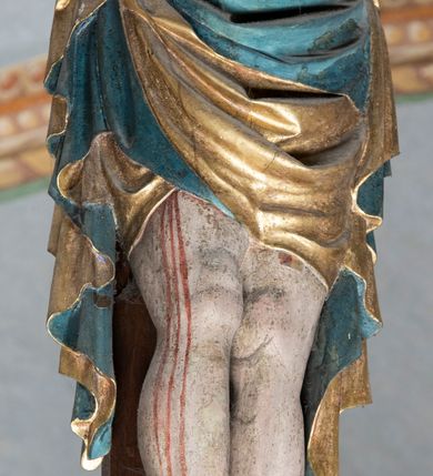 Zdjęcie nr 3: Rzeźba pełnoplastyczna, z tyłu opracowana. Ciało Chrystusa przybite do krzyża na niemal horyzontalnie, szeroko rozłożonych ramionach. Głowa w koronie cierniowej pochylona na prawe ramię. Długie włosy w puklach o spiralnie zakończonych lokach opadają na ramiona i plecy. Twarz szczupła o zindywidualizowanych rysach, pełna spokoju i smutku, okolona krótkim zarostem, z wydatnymi kośćmi policzkowymi, z kroplami krwi na czole. Duże, okrągłe oczy przesłonięte powiekami, podkreślone uniesionymi łukami brwiowymi. Usta drobne, zaciśnięte, nos prosty, wąski. Ręce chude długie, silnie wyprężone, dłonie rozchylone, przebite gwoździami. Klatka piersiowa o starannie opracowanej anatomii, z silnym wcięciem w talii oraz raną w prawym boku. Perizonium w kształcie chusty, sięgające do połowy uda, miękko udrapowane z przodu, spływające po obu bokach kaskadowymi fałdami. Nogi wyprostowane, umięśnione, ułożone obok siebie, stopy stosunkowo duże, skrzyżowane, założone prawa na lewą, przebite jednym gwoździem. Z ran na boku, dłoniach i stopach spływa obficie krew. Karnacja Chrystusa jasnoróżowa, włosy brązowe z domalowanym warkoczem z tyłu, korona zielona, perizonium złocone, z niebieską podszewką. Krzyż łaciński, dębowy, w naturalnym kolorze drewna, wykonany w 1890, w formie Drzewa Życia, z rozłożystymi liśćmi uschniętego akantu w kolorze czerwonym i złotym żyłkowaniem na skrzyżowaniu ramion. W zakończeniu ramion lilijki czerwono-zielone ze złoconymi obwódkami oraz nakładane plakiety w układzie koncentrycznym tworzące ośmioramienne gwiazdy z płaskorzeźbionymi symbolami Ewangelistów. Tła plakiet malowane na niebiesko, symbole i obramienia złocone. Plakiety współczesne z rzeźbą Chrystusa, gotyckie - 1433 r.; u góry krzyża - symbol św. Jana - orzeł, u dołu - symbol św. Łukasza - wół, na prawym ramieniu symbol św. Mateusza - anioł, na lewym ramieniu - symbol św. Marka - lew. Ponad głową Chrystusa titulus z napisem: INRI. Plakieta kwadratowa nałożona na romb w układzie koncentrycznym, w profilowanym obramieniu, z płaskorzeźbionym przedstawieniem orła; u dołu banderola z napisem minuskułą gotycką: sanctus joannes. Plakieta kwadratowa nałożona na romb w układzie koncentrycznym, w obramieniu profilowanym, z fazą wklęsłą - z płaskorzeźbionym przedstawieniem anioła w pozycji siedzącej z podkurczonymi nogami w ujęciu frontalnym, w rękach podtrzymującego faliście wygiętą banderolę o zrolowanych zakończeniach, z czarnym napisem minuskułą gotycką: sanctus matheus; banderola biała z czarnymi rozetkami. Twarz anioła okrągła, o rysach dziecka, różowa, okolona puklami rudych włosów. Anioł ubrany w fałdzistą szatę, złoconą z trójkątnym dekoltem, udrapowaną na kolanach w głębokie, łyżkowate fałdy. U ramion szeroko rozpostarte skrzydła o schematycznych rombowych podziałach, zagięte na brzegach, zakończone długimi piórami, lotkami - złocone. Tło lekko pogłębione, niebieskie; obramienia kwadratów złocone, boki i tylne ściany malowane na brązowo. Plakieta kwadratowa nałożona na romb w układzie koncentrycznym, w obramieniu profilowanym, z fazą wklęsłą, z płaskorzeźbionym przedstawieniem uskrzydlonego wołu, w pełnej postaci, w ujęciu bocznym, o masywnej budowie ciała, w dynamicznym ruchu, wspartego na rozstawionych nogach, zakończonych ciężkimi kopytami, z puszystym ogonem. Głowa zwrócona na wprost, oczy duże, nozdrza rozdęte, uszy odstające na boki, pośrodku ozdobnie osadzone esowato wygięte rogi. Skrzydła wyrastające z barków, uniesione w górę, rozpostarte, upierzenie schematyczne zaznaczone w kształcie rombów, z długimi lotkami w zakończeniach wygiętych skrzydeł. U dołu, pomiędzy nogami zwierzęcia - półkoliście wygięta biała banderola, z czarnym napisem minuskułą gotycką: sanctus lucas i czarnymi rozetkami. Tło nieco pogłębione, niebieskie. Postać wołu, obramienie plakiet, złocone; ścianki tylne malowane na brązowo. Plakieta w kształcie rombu nałożonego na kwadrat w układzie koncentrycznym, w obramieniu profilowanym, z fazą wklęsłą - z płaskorzeźbionym przedstawieniem uskrzydlonego lwa. W pełnej postaci, ujęciu bocznym, muskularnych kształtach, mocnych nogach z potężnymi pazurami. Głowa zwrócona na wprost, ujęta bujną, silnie skręconą grzywą. Skrzydła wyrastające z barków uniesione w górę, szeroko rozpostarte, zakończone długimi lotkami; upierzenie schematycznie zaznaczone w formie regularnych rombów. Ogon cienki, długi, z puszystą kitką, przechodzący pomiędzy nogami, esowato wygięty nad grzbietem. U dołu biała banderola, podtrzymywana pazurami przednich łap, z napisem czarnym, gotycką minuskułą: sanctus marcus i czarnymi rozetkami. Tło nieco pogłębione, niebieskie; postać lwa i obramienia złocone, tylne ścianki malowane na brązowo.