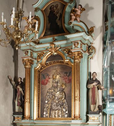 Zdjęcie nr 5: Rzeźba pełnoplastyczna, ustawiona na podstawie na planie prostokąta. Święty Dominik ukazany frontalnie, w kontrapoście, z pochyloną głową, prawą rękę kładzie na piersi, w lewej wyciągniętej do przodu trzyma różaniec. Twarz o wyraźnie zaznaczonych zmarszczkach, dużych uszach, zapadniętych policzkach, zmarszczonym czole, o dużych oczach skierowanych w dół, wydatnym nosie i wąskich ustach z gęstymi wąsami. Włosy ma krótkie, brązowe, z tonsurą na głowie. Święty ubrany jest w biały habit ze złoconą lamówką, przepasany w talii, z różowym szkaplerzem, na ramiona ma narzuconą brązową pelerynkę z kapturem i złoconą lamówką. Polichromia ciała naturalistyczna, o bladej karnacji. Przy lewej nodze świętego postać brązowego, leżącego psa. 



