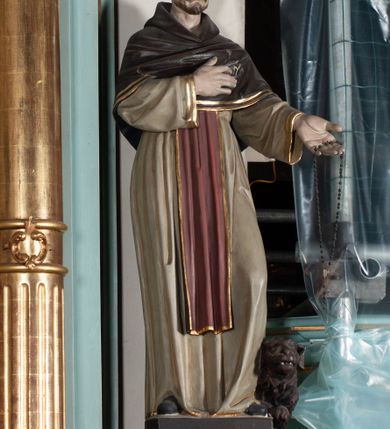 Zdjęcie nr 3: Rzeźba pełnoplastyczna, ustawiona na podstawie na planie prostokąta. Święty Dominik ukazany frontalnie, w kontrapoście, z pochyloną głową, prawą rękę kładzie na piersi, w lewej wyciągniętej do przodu trzyma różaniec. Twarz o wyraźnie zaznaczonych zmarszczkach, dużych uszach, zapadniętych policzkach, zmarszczonym czole, o dużych oczach skierowanych w dół, wydatnym nosie i wąskich ustach z gęstymi wąsami. Włosy ma krótkie, brązowe, z tonsurą na głowie. Święty ubrany jest w biały habit ze złoconą lamówką, przepasany w talii, z różowym szkaplerzem, na ramiona ma narzuconą brązową pelerynkę z kapturem i złoconą lamówką. Polichromia ciała naturalistyczna, o bladej karnacji. Przy lewej nodze świętego postać brązowego, leżącego psa. 



