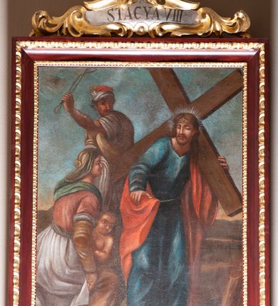 Zdjęcie nr 11: Stacje drogi krzyżowej zawieszone na ścianach bocznych nawy głównej. Obrazy w kształcie stojących prostokątów. W zwieńczeniu w kartuszu oplecionym rzeźbionymi liśćmi akantu malowane nazwy stacji, zapisane „STACYA I / STACYA II [...]”. U góry zakończone krzyżykiem łacińskim. Obrazy ujęte profilowaną ramą, zdobioną kimationem.  Kolorystyka żywa, z dominacją czerwieni i błękitu, plan dalszy rozmyty. Rama polichromowana na bordowo, profilowania i ornamentyka złocone, detale srebrzone.
