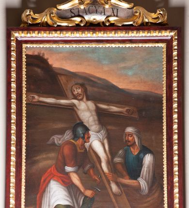 Zdjęcie nr 3: Stacje drogi krzyżowej zawieszone na ścianach bocznych nawy głównej. Obrazy w kształcie stojących prostokątów. W zwieńczeniu w kartuszu oplecionym rzeźbionymi liśćmi akantu malowane nazwy stacji, zapisane „STACYA I / STACYA II [...]”. U góry zakończone krzyżykiem łacińskim. Obrazy ujęte profilowaną ramą, zdobioną kimationem.  Kolorystyka żywa, z dominacją czerwieni i błękitu, plan dalszy rozmyty. Rama polichromowana na bordowo, profilowania i ornamentyka złocone, detale srebrzone.
