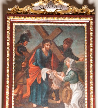 Zdjęcie nr 10: Stacje drogi krzyżowej zawieszone na ścianach bocznych nawy głównej. Obrazy w kształcie stojących prostokątów. W zwieńczeniu w kartuszu oplecionym rzeźbionymi liśćmi akantu malowane nazwy stacji, zapisane „STACYA I / STACYA II [...]”. U góry zakończone krzyżykiem łacińskim. Obrazy ujęte profilowaną ramą, zdobioną kimationem.  Kolorystyka żywa, z dominacją czerwieni i błękitu, plan dalszy rozmyty. Rama polichromowana na bordowo, profilowania i ornamentyka złocone, detale srebrzone.
