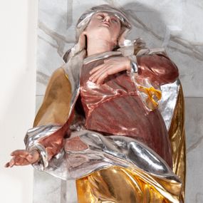 Zdjęcie nr 1: Figura drążona, silnie ścięta z tyłu, przedstawiająca św. Annę. Święta ustawiona frontalnie, w kontrapoście, z prawą nogą ugiętą w kolanie i wspartą na stopniu, o silnie skręconej sylwetce, z lewą ręką złożoną na piersi, prawą odsuniętą w bok. Głowa skierowana w górę, delikatnie przechylona na lewe ramię. Twarz szczupła o wyraźnych rysach, oczy zwrócone ku górze, usta rozchylone. Święta jest ubrana w długą, czerwoną suknię, przepasaną w talii, u spodu obficie marszczoną oraz złocony płaszcz, srebrzony na podbiciu, założony na głowę, opadający na plecy i ramiona, zawinięty na prawej nodze; obficie drapowany. W partiach ciała polichromia naturalistyczna, płaszcz złocony, podbicie srebrzone.