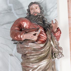 Zdjęcie nr 1: Figura drążona, mocno ścięta z tyłu, przedstawiająca św. Joachima. Święty ustawiony frontalnie, lewa ręka uniesiona i wysunięta przed siebie, a prawą, ugiętą podtrzymuje przy boku księgę. Głowę ma skierowaną w prawą stronę, delikatnie pochyloną. Twarz szeroka z długim nosem o niewielkich oczach patrzących w bok oraz delikatnie rozchylonych ustach; okolona długą brodą w postaci silnie skręconych dwóch pukli opadających diagonalnie na pierś. Włosy długie z przedziałkiem na środku głowy, kręcone, opadają na plecy i lewe ramię. Święty ubrany jest w czerwoną, silnie przylegającą do ciała suknię z wąskimi rękawami oraz brązowy płaszcz przerzucony przez lewe ramię, opadający przez plecy, otaczający postać i odsłaniający klatkę piersiową. Tkanina ekspresyjnie drapowana, obficie fałdowana z rozwianym spodem. Polichromia naturalistyczna w partiach ciała.