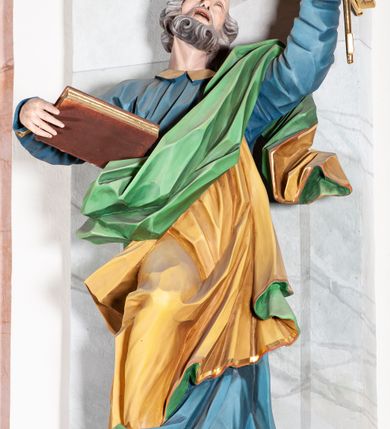 Zdjęcie nr 3: Rzeźba drążona, ścięta z tyłu, przedstawiająca św. Piotra. Święty ustawiony frontalnie, o esowato wygiętej sylwetce, z ugiętą prawą nogą, opartą o stopień. W lewej uniesionej wysoko ręce trzyma dwa klucze, prawą  podtrzymuje opartą o bok księgę. Głowa skierowana trzy czwarte w lewo i uniesiona w górę. Twarz ascetyczna, oczy uniesione w górę, rozchylone usta; okolona gęstą brodą, układającą się w pukle. Włosy siwe w postaci silnie skręconych loków po bokach i na tyle głowy oraz pukiel na czole. Święty ubrany jest w niebieską suknię z kołnierzykiem oraz przerzucony diagonalnie przez lewe ramię żółty płaszcz ze złoconą lamówką i zieloną podszewką. Tkanina ekspresyjnie kształtowana, silnie drapowana, miejscami przylegająca do ciała. Polichromia naturalistyczna, atrybuty i lamówka złocone.