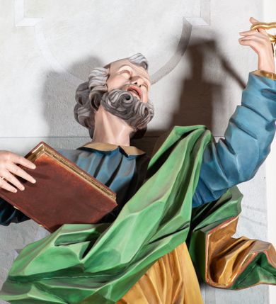 Zdjęcie nr 4: Rzeźba drążona, ścięta z tyłu, przedstawiająca św. Piotra. Święty ustawiony frontalnie, o esowato wygiętej sylwetce, z ugiętą prawą nogą, opartą o stopień. W lewej uniesionej wysoko ręce trzyma dwa klucze, prawą  podtrzymuje opartą o bok księgę. Głowa skierowana trzy czwarte w lewo i uniesiona w górę. Twarz ascetyczna, oczy uniesione w górę, rozchylone usta; okolona gęstą brodą, układającą się w pukle. Włosy siwe w postaci silnie skręconych loków po bokach i na tyle głowy oraz pukiel na czole. Święty ubrany jest w niebieską suknię z kołnierzykiem oraz przerzucony diagonalnie przez lewe ramię żółty płaszcz ze złoconą lamówką i zieloną podszewką. Tkanina ekspresyjnie kształtowana, silnie drapowana, miejscami przylegająca do ciała. Polichromia naturalistyczna, atrybuty i lamówka złocone.