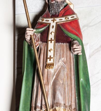 Zdjęcie nr 2: Rzeźba pełna, przedstawiająca św. Klemensa, ustawiona na niskim prostopadłościennym cokole. Święty ustawiony frontalnie w sztywnej pozie, z lewą nogą delikatnie ugiętą w kolanie, z pastorałem w prawej dłoni i lewą ręką wysuniętą do przodu. Twarz podłużna o delikatnie rozchylonych ustach, długim nosie, okolona falowaną brodą. Święty jest ubrany w malowaną na złoto albę, jasnoróżową komżę, bordowy mucet, czerwoną kapę z zieloną podszewką oraz biały paliusz. Na głowie ma założoną czerwoną infułę, a na stopach ciemnobrązowe buty. Polichromia naturalistyczna, detale stroju i pastorał złocone.