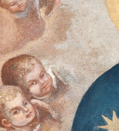 Zdjęcie nr 7: Obraz w formie stojącego prostokąta zamkniętego łukiem półkolistym z przedstawieniem Matki Boskiej Śnieżnej. W centrum kompozycji została ukazana Matka Boska z Dzieciątkiem w ujęciu do kolan, frontalnie. Maria oburącz podtrzymuje siedzące na jej lewym przedramieniu Dzieciątko, a w lewej dłoni trzyma białą chusteczkę. Twarz Marii pełna o delikatnie zarysowanych oczach i długim, prostym nosie oraz małych ustach. Ubrana jest w czerwoną suknię oraz ciemnogranatowy płaszcz zarzucony na głowę i ramiona ze złotą lamówką i gwiazdą na prawym ramieniu. Dzieciątko zwrócone jest trzy czwarte w prawo, głowę delikatnie unosi ku górze w stronę Matki. W lewej ręce trzyma zamkniętą księgą w czerwonej oprawie, a prawą błogosławi. Twarz o dziecięcych rysach z zarumienionymi policzkami. Włosy krótkie, jasne i kędzierzawe. Ubrane jest w białą sukienkę oraz sandały. Oboje wokół głów mają złote i koliste nimby. Nad głową Matki Boskiej znajduje się para aniołków, które podtrzymują zamkniętą koronę. Całość ukazana jest na tle obłoków, po bokach są uskrzydlone główki aniołków. Rama drewniana, profilowana i złocona.