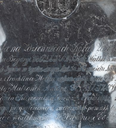 Zdjęcie nr 1: Tablica w kształcie leżącego prostokąta, zwieńczona medalionem, w którym znajduje się tarcza herbowa, dzielona w słup z dwoma godłami: po prawej błędnie odkute godło herbu Bogoria (przekrzyżowana rogacina na wspak), po lewej godło herbu Korab, nad tarczą korona otwarta. W polu inskrypcja „Józefa na Zdziennicach Korab Zdzieńska / Zamężna na Bogoryi de PLESZOWSKA Matka 5. małoletnich / pozostałych Synów w życiu swym Lat 30. w Zamęściu Lat 13. Cnotliwa / Małżonka i troskliwa Matka zakończyła życie d(nia) 2 List(opada) 1821 r(oku) / Pozostały Małżonek Antoni de PLESZOWSKI / C(esarski) [i] K(rólewski) Sędzia Kameralny wraz z Familią w dowód / prawdziwego przywiązania i szacunku pomnik ten położył / prosząc o westchnienie za Jey Duszę do BOGA.”
