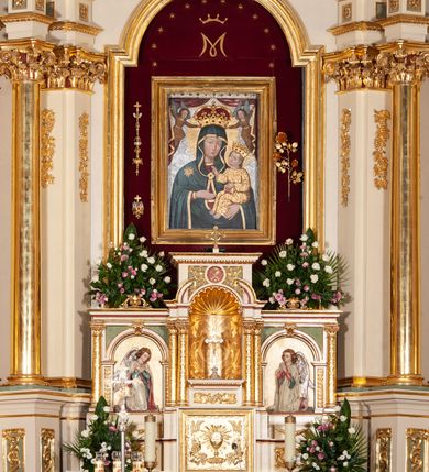 Zdjęcie nr 2: Tabernakulum architektoniczne, trójosiowe, na wysokim cokole. Oś środkowa wyższa od bocznych. U jej podstawy prostokątne, złocone drzwiczki ujęte profilowaną ramą. Na froncie odlewana dekoracja w postaci kielicha z hostią w glorii promienistej w otoczeniu  kłosów oraz winnych gron. Powyżej nisza na Tron Wystawienia zamknięta muszlą oraz rytą dekoracją akantową ujmującą medalion z inskrypcją IHS.  Niszę ujmuje para zdwojonych, korynckich kolumn o złoconych trzonach dekorowanych ornamentem roślinnym, dźwigających odcinki pełnego belkowania oraz półkolistego przerwanego przyczółka. Pomiędzy odcinkami przyczółka cokół zamknięty gzymsem dekorowanym jajownikiem, od frontu zdobiony medalionem z Chrismonem,  ujętym płycinami z akantem. Osie skrajne ujęte analogicznymi kolumnami mieszczą arkady o węgarach dekorowanych cekinami; z wolutowym kluczem. W polach antytetycznie ustawione płaskorzeźbione, polichromowane i srebrzone figury klęczących i modlących się aniołów. Osie zwieńczone profilowanym gzymsem, na którym dekoracja z wolutowo skręconego akantu. Struktura malowana na jasno-beżowo oraz zielono. Ornamentyka oraz tła złocone.