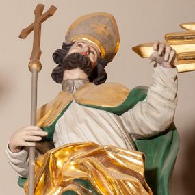Zdjęcie nr 1: Rzeźba pełnoplastyczna, figura zwrócona trzy czwarte w lewo, ustawiona w pozycji stojącej w silnym kontrapoście, z prawą nogą ugiętą w kolanie, z głową przechyloną w lewą stronę. W prawej ręce trzyma krzyż od długim drzewcu, lewą wyciąga przed siebie. Twarz szeroka, o spiczastym nosie, okolona krótką i ciemnobrązową brodą. Włosy średniej długości, ciemnobrązowe, zasłaniające uszy. Święty ubrany jest w brązową albę, białą komżę oraz złoty płaszcz z zieloną podszewką, spięty na piersi, z silnie drapowaną prawą połą. Na głowie ma srebrzoną infułę ze złoconym krzyżem. Polichromia naturalistyczna, detale stroju złocone.
