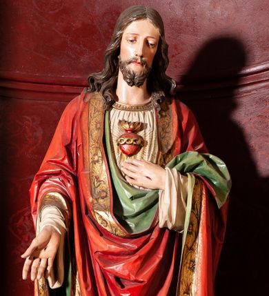 Zdjęcie nr 1: Rzeźba pełna, ustawiona frontalnie na niskim, zielonym postumencie. Chrystus stoi w delikatnym kontrapoście, lewą ręką wskazuje na gorejące na piersi serce, prawą opuszczoną w dół, ukazuje ranę na dłoni. Ma podłużną twarz, z delikatnie przymkniętymi oczami, długim i wąskim nosem, okoloną krótką brodą zakończoną w dwa pukle; włosy długie, z przedziałkiem  na środku głowy, opadają na ramiona w postaci loków. Chrystus ubrany jest w długą, sięgającą stóp, białą i silnie drapowaną suknię, o szerokich rękawach, ze złotą lamówką pod szyją. Na ramiona ma narzucony czerwony płaszcz, podtrzymywany lewą ręką, z dekorowaną i złoconą bordiurą oraz zielonym podbiciem. Polichromia naturalistyczna w odsłoniętych partiach ciała, detal stroju złocony.