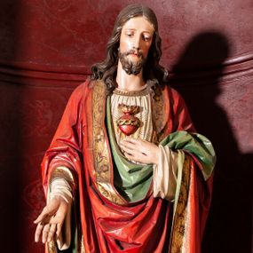 Zdjęcie nr 1: Rzeźba pełna, ustawiona frontalnie na niskim, zielonym postumencie. Chrystus stoi w delikatnym kontrapoście, lewą ręką wskazuje na gorejące na piersi serce, prawą opuszczoną w dół, ukazuje ranę na dłoni. Ma podłużną twarz, z delikatnie przymkniętymi oczami, długim i wąskim nosem, okoloną krótką brodą zakończoną w dwa pukle; włosy długie, z przedziałkiem  na środku głowy, opadają na ramiona w postaci loków. Chrystus ubrany jest w długą, sięgającą stóp, białą i silnie drapowaną suknię, o szerokich rękawach, ze złotą lamówką pod szyją. Na ramiona ma narzucony czerwony płaszcz, podtrzymywany lewą ręką, z dekorowaną i złoconą bordiurą oraz zielonym podbiciem. Polichromia naturalistyczna w odsłoniętych partiach ciała, detal stroju złocony.