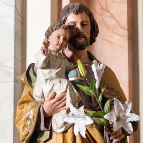 Zdjęcie nr 1: Rzeźba pełna, ustawiona na prostopadłościennym cokole o ściętych narożach. Święty Józef został ukazany w postawie stojącej, w delikatnym kontrapoście, z Dzieciątkiem Jezus na prawym ręku, w lewej ręce, wyciągniętej przed siebie trzyma gałązkę białej lilii. Ma twarz okoloną krótką brodą, małe usta i długi nos. Włosy średniej długości, ciemnobrązowe, zasłaniają uszy. Święty Józef ubrany jest w fioletową, długą suknię z długimi rękawami oraz jasnobrązowy płaszcz, na brzegu zdobiony stylizowaną wicią roślinną. Dzieciątko Jezus zwrócone jest trzy czwarte w lewo, w pozycji siedzącej, z prawą ręką wzniesioną w geście błogosławieństwa, lewą wspartą na jabłku królewskim. Ubrane jest w długą, białą sukienkę, obwiedzioną na brzegach złotą lamówką. Polichromia w odsłoniętych partiach ciała naturalistyczna. 



