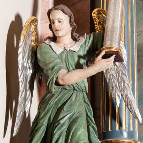 Zdjęcie nr 1: Rzeźba pełnoplastyczna, drążona, przedstawiająca anioła z arma Christi w dłoniach. Figura ustawiona frontalnie z lewą nogą wysuniętą do przodu, z głową skierowaną w prawą stronę. W uniesionych po swojej lewej stronie dłoniach trzyma kolumnę biczowania. Twarz szeroka z wysokim czołem, prostym nosem, wzrokiem skierowanym w dół i delikatnie rozchylonymi ustami. Włosy długie, ciemnobrązowe z przedziałkiem pośrodku, opadające na ramiona.  Anioł jest ubrany w czerwoną, długą szatę spodnią, silnie drapowaną, na niej ma założoną zieloną tunikę z białym kołnierzykiem, na stopach pomarańczowe, rzymskie sandały. Kolumna ustawiona na bazie, trzon gładki, kapitel koryncki. Polichromia naturalistyczna, skrzydła posrebrzane i pozłacane.