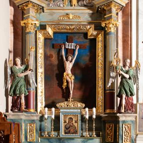 Zdjęcie nr 1: Ołtarz przyścienny, architektoniczny, jednoosiowy, jednokondygnacyjny, ze zwieńczeniem. Mensa ołtarzowa skrzyniowa, prostopadłościenna, z portatylem w formie kamiennej płyty. Antepedium współczesne, ujęte profilowaną ramą zdobioną żłobionym wałkiem, obite blachą miedzianą, na której odlewana, aplikowana dekoracja przedstawiająca w centrum Baranka Bożego w glorii promienistej z obłokami, po bokach dwie klęczące postacie kobiece, symbole ewangelistów oraz motywy kwiatowe. Nastawa ołtarzowa na podwójnym cokole, flankowana dwiema kanelowanymi od jednej czwartej wysokości kolumnami o kapitelach kompozytowych, dźwigających pełne i wyłamane belkowanie oraz imposty ustawione pod kątem, na których znajduje się para puttów z arma Christi. Po zewnętrznej stronie kolumn cokoły z figurami aniołów. Pole środkowe w formie niszy w kształcie stojącego prostokąta o wciętych górnych narożach, gdzie na tle malowanego pejzażu znajduje się rzeźbiony krucyfiks. Zwieńczenie w formie promienistej glorii z otoczonym obłokami medalionem, w którego polu monogram IHS. Cokoły figur i kolumn dekorowane płycinami z esowato wygiętym ornamentem roślinnym. Gzyms impostów zdobiony ornamentem roślinnym, w partii fryzu rzeźbiona uskrzydlona główka anielska. Rama w polu środkowym dekorowana płaskorzeźbionym ornamentem roślinnym. Struktura marmoryzowana w odcieniu różowo-błękitnym, detale architektoniczne polichromowane na niebiesko i czerwono, ornamentyka i profilowania pozłacane i posrebrzane.