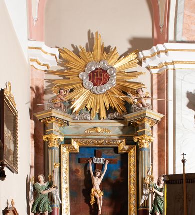 Zdjęcie nr 2: Ołtarz przyścienny, architektoniczny, jednoosiowy, jednokondygnacyjny, ze zwieńczeniem. Mensa ołtarzowa skrzyniowa, prostopadłościenna, z portatylem w formie kamiennej płyty. Antepedium współczesne, ujęte profilowaną ramą zdobioną żłobionym wałkiem, obite blachą miedzianą, na której odlewana, aplikowana dekoracja przedstawiająca w centrum Baranka Bożego w glorii promienistej z obłokami, po bokach dwie klęczące postacie kobiece, symbole ewangelistów oraz motywy kwiatowe. Nastawa ołtarzowa na podwójnym cokole, flankowana dwiema kanelowanymi od jednej czwartej wysokości kolumnami o kapitelach kompozytowych, dźwigających pełne i wyłamane belkowanie oraz imposty ustawione pod kątem, na których znajduje się para puttów z arma Christi. Po zewnętrznej stronie kolumn cokoły z figurami aniołów. Pole środkowe w formie niszy w kształcie stojącego prostokąta o wciętych górnych narożach, gdzie na tle malowanego pejzażu znajduje się rzeźbiony krucyfiks. Zwieńczenie w formie promienistej glorii z otoczonym obłokami medalionem, w którego polu monogram IHS. Cokoły figur i kolumn dekorowane płycinami z esowato wygiętym ornamentem roślinnym. Gzyms impostów zdobiony ornamentem roślinnym, w partii fryzu rzeźbiona uskrzydlona główka anielska. Rama w polu środkowym dekorowana płaskorzeźbionym ornamentem roślinnym. Struktura marmoryzowana w odcieniu różowo-błękitnym, detale architektoniczne polichromowane na niebiesko i czerwono, ornamentyka i profilowania pozłacane i posrebrzane.