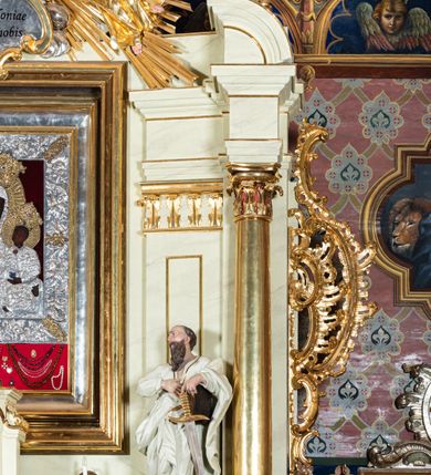 Zdjęcie nr 20: Nastawa ołtarzowa jednoosiowa, jednokondygnacyjna ze zwieńczeniem, na podwójnym cokole. W partii cokołu prostokątne płyciny, z których wewnętrzne są wypełnione wotami.  Mensa drewniana, wklęsło-wypukła. Kondygnacja nastawy ujęta szerokimi pilastrami o kapitelach zdobionych liśćmi akantu ustawionymi skośnie oraz stojącą przed nimi parą kolumn. Podpory dźwigają fragmenty pełnego belkowania wyłamanego na ich osiach; przerwanego nad polem środkowym. Kolumny podtrzymują przerwany przyczółek, na którym ustawiono fragmenty dekoracji rokokowej. Podpory ustawione zostały na profilowanych cokołach, po ich wewnętrznych stronach figury św. Piotra po lewej i św. Pawła po prawej stronie. W polu środkowym obraz z przedstawieniem Matki Boskiej Częstochowskiej w profilowanej ramie w kształcie stojącego prostokąta Nad nia kartusz z napisem „Regina Poloniae / ora pro nobis”. Kondygnacje ujmują uszaki z płomienistego rocaille’a.  Zwieńczenie tworzy rzeźbiarska grupa Trójcy świętej na obłokach, między którymi unoszą się uskrzydlone główki anielskie. Struktura polichromowana na kremowo, kolumny złocone, detale, profile i ornamenty złocone i srebrzone. 