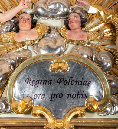 Zdjęcie nr 8: Nastawa ołtarzowa jednoosiowa, jednokondygnacyjna ze zwieńczeniem, na podwójnym cokole. W partii cokołu prostokątne płyciny, z których wewnętrzne są wypełnione wotami.  Mensa drewniana, wklęsło-wypukła. Kondygnacja nastawy ujęta szerokimi pilastrami o kapitelach zdobionych liśćmi akantu ustawionymi skośnie oraz stojącą przed nimi parą kolumn. Podpory dźwigają fragmenty pełnego belkowania wyłamanego na ich osiach; przerwanego nad polem środkowym. Kolumny podtrzymują przerwany przyczółek, na którym ustawiono fragmenty dekoracji rokokowej. Podpory ustawione zostały na profilowanych cokołach, po ich wewnętrznych stronach figury św. Piotra po lewej i św. Pawła po prawej stronie. W polu środkowym obraz z przedstawieniem Matki Boskiej Częstochowskiej w profilowanej ramie w kształcie stojącego prostokąta Nad nia kartusz z napisem „Regina Poloniae / ora pro nobis”. Kondygnacje ujmują uszaki z płomienistego rocaille’a.  Zwieńczenie tworzy rzeźbiarska grupa Trójcy świętej na obłokach, między którymi unoszą się uskrzydlone główki anielskie. Struktura polichromowana na kremowo, kolumny złocone, detale, profile i ornamenty złocone i srebrzone. 