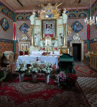 Zdjęcie nr 5: Nastawa ołtarzowa jednoosiowa, jednokondygnacyjna ze zwieńczeniem, na podwójnym cokole. W partii cokołu prostokątne płyciny, z których wewnętrzne są wypełnione wotami.  Mensa drewniana, wklęsło-wypukła. Kondygnacja nastawy ujęta szerokimi pilastrami o kapitelach zdobionych liśćmi akantu ustawionymi skośnie oraz stojącą przed nimi parą kolumn. Podpory dźwigają fragmenty pełnego belkowania wyłamanego na ich osiach; przerwanego nad polem środkowym. Kolumny podtrzymują przerwany przyczółek, na którym ustawiono fragmenty dekoracji rokokowej. Podpory ustawione zostały na profilowanych cokołach, po ich wewnętrznych stronach figury św. Piotra po lewej i św. Pawła po prawej stronie. W polu środkowym obraz z przedstawieniem Matki Boskiej Częstochowskiej w profilowanej ramie w kształcie stojącego prostokąta Nad nia kartusz z napisem „Regina Poloniae / ora pro nobis”. Kondygnacje ujmują uszaki z płomienistego rocaille’a.  Zwieńczenie tworzy rzeźbiarska grupa Trójcy świętej na obłokach, między którymi unoszą się uskrzydlone główki anielskie. Struktura polichromowana na kremowo, kolumny złocone, detale, profile i ornamenty złocone i srebrzone. 