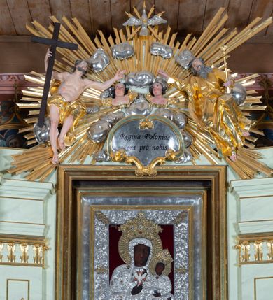 Zdjęcie nr 6: Nastawa ołtarzowa jednoosiowa, jednokondygnacyjna ze zwieńczeniem, na podwójnym cokole. W partii cokołu prostokątne płyciny, z których wewnętrzne są wypełnione wotami.  Mensa drewniana, wklęsło-wypukła. Kondygnacja nastawy ujęta szerokimi pilastrami o kapitelach zdobionych liśćmi akantu ustawionymi skośnie oraz stojącą przed nimi parą kolumn. Podpory dźwigają fragmenty pełnego belkowania wyłamanego na ich osiach; przerwanego nad polem środkowym. Kolumny podtrzymują przerwany przyczółek, na którym ustawiono fragmenty dekoracji rokokowej. Podpory ustawione zostały na profilowanych cokołach, po ich wewnętrznych stronach figury św. Piotra po lewej i św. Pawła po prawej stronie. W polu środkowym obraz z przedstawieniem Matki Boskiej Częstochowskiej w profilowanej ramie w kształcie stojącego prostokąta Nad nia kartusz z napisem „Regina Poloniae / ora pro nobis”. Kondygnacje ujmują uszaki z płomienistego rocaille’a.  Zwieńczenie tworzy rzeźbiarska grupa Trójcy świętej na obłokach, między którymi unoszą się uskrzydlone główki anielskie. Struktura polichromowana na kremowo, kolumny złocone, detale, profile i ornamenty złocone i srebrzone. 