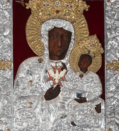 Zdjęcie nr 1: Obraz w kształcie stojącego prostokąta z przedstawieniem Matki Boskiej z Dzieciątkiem w typie Częstochowskiej, w srebrnej sukience odsłaniającej jedynie twarze i dłonie, otoczony szeroką bordiurą z repusowaną dekoracją floralną. Matka Boska ukazana frontalnie z Dzieciątkiem na lewym ręku, prawą rękę ma złożoną na piersi. Twarze o ciemnych karnacjach. Matka Boska delikatnie zwraca głowę w lewo, ma wzrok skierowany w dal, długi i wąski nos, na prawym policzku dwie blizny. Dzieciątko ukazane w pozycji siedzącej, z prawą rączką wzniesioną w geście błogosławieństwa, w lewej trzyma na kolanach zamkniętą księgę. Sukienki drewniane, płaszcz Matki Boskiej bogato dekorowany roślinną dekoracją. Wokół głów obu postaci złote, koliste nimby promieniste z nałożonymi, bardzo ozdobnymi, również złotymi koronami utworzonymi z ornamentu roślinnego dekorowanego kameryzacją. Sukienki obu postaci srebrne, również zdobione ornamentem roślinnym i kameryzacją, na dekolcie Marii aplikowany order Orła Białego. Tło obrazu stanowi ciemnoczerwona tkanina. Przedstawienie obwiedzione szerokim, metalowym pasem srebrnej dekoracji floralnej ze złoconymi plakietami w narożach i połowie wysokości każdego boku ramy. U góry zawieszono rząd orderów, po bokach serca wotywne, na dolnej krawędzi liczne sznury korali. 