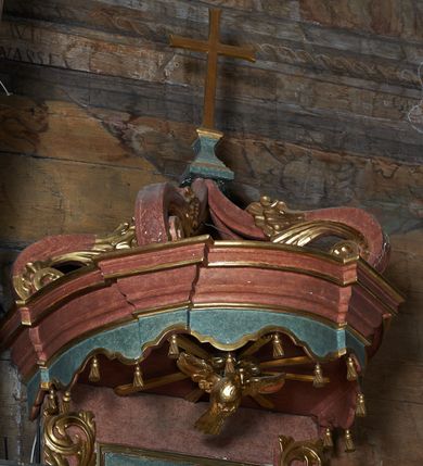 Zdjęcie nr 3: Ambona zawieszona na północnej ścianie prezbiterium. Kosz na rzucie owalu, z wydzielonym profilowanym cokołem i gzymsem, opięty wolutami umieszczonymi na tle pilastrów; wsparty na nadwieszonej podstawie o formie odwróconego spłaszczonego stożka, ujętego pięcioma wolutowo wygiętymi kabłąkami. Zaplecek prostokątny, łączący się z owalnym baldachimem zwieńczonym krzyżem ustawionym na czterech kabłąkach. Baldachim od dołu dekorowany lambrekinem. Od strony wschodniej schody z balustradą zdobioną romboidalnymi płycinami z aplikowanym ornamentem roślinnym. Płyciny kosza oraz boki zaplecka dekorowane wicią akantu. Pośrodku zaplecka płaskorzeźbiona figura Chrystusa Dobrego Pasterza, w podniebiu rzeźbiona Gołębica Ducha Świętego otoczona promieniami. Całość struktury ambony polichromowana na kolor ciemnobrązowy oraz ciemnozielony w partii płycin, detal i profilowania pozłacane.