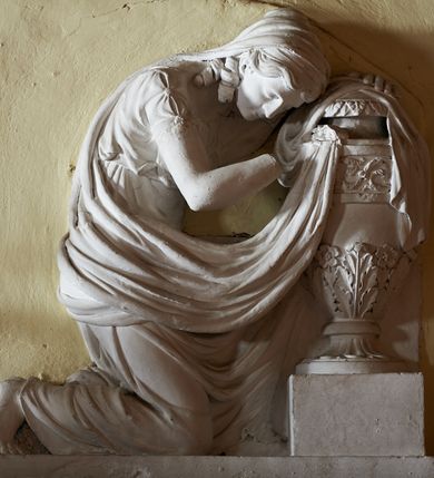 Zdjęcie nr 3: Wmurowany w ścianę kościoła nagrobek, na wysokim postumencie, z tablicą w kształcie leżącego prostokąta z czterema metalowymi ćwiekami w kształcie rozet, w szerokiej ramie z stiukowymi herbami Nowina i Bogoria na bokach i profilowanym gzymsem z czterema stiukowymi rozetami. Ponad gzymsem ukazana z prawego profilu klęcząca i wsparta na urnie kobieta, ubrana w togę i płaszcz zarzucony na głowę, plecy i częściowo zakrywający urnę, na której kobieta wspiera ręce i głowę. Twarz pełna, o delikatnych rysach i zamkniętych oczach. Włosy sięgające ramion, o gęstych, kręconych puklach. Urna w typie amfory greckiej zdobiona dołem szerokimi liśćmi i pięciopłatkowymi kwiatami, górą fryzem z liśćmi akantu. Na tablicy inskrypcja: &quot;D(eo) O(ptimo) M(aximo) / Józefowi i Teressie Skotnickich / KONOPKOM. / Łowczym Sanockim / Rodzicom Dobrodziejom Naszym. / Teressie w dniu 15. Grudnia 1801. a Józefowi / d(nia) 27. Września 1811. R(oku) zmarłym / Pomnik kładziemy&quot;. 