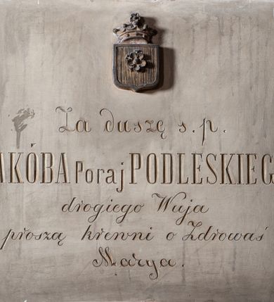 Zdjęcie nr 1: Tablica pamiątkowa, kamienna, kwadratowa, z inskrypcją po polsku, ozdobnymi złoconymi literami: Za duszę s. p. / JAKÓBA Poraj PODLESKIEGO / drogiego Wuja / proszą krewni o Zdrowaś / Marya. Pośrodku, ponad inskrypcją, aplikowana tarcza pod koroną otwartą, z herbem Poraj.
