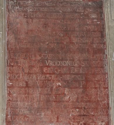 Zdjęcie nr 3: Tablica w kształcie stojącego prostokąta, w ozdobnej, uszatej ramie, podtrzymywana po bokach przez dwie, płaskorzeźbione postacie, zwieńczona kartuszem z herbami: Dołęga, Śreniawa i Radwan. W polu marmurowa prostokątna płyta z majuskułową inskrypcją w języku polskim, częściowo nieczytelną: BÓG W TRÓJCY JEDYNEMU NASWIETSZY PANNIE / MIESZKANCZOM WSZYSTKIM NIEBA TAKŻE S. ANNIE / NA CZESC I CHWALE (...) ZBUDOWAĆ KAZAŁ  / KATARZINA KUCHARsKA CHCĄC BY SIĘ TU CHWAŁA / PAŃSKA SZERZEŁA ZAWSZE PÓKI LUDZKIE PLEMIĘ  / OSIADAĆ BĘDZIE (...) WSZYSTKO RODNĄ ZIEMIĘ  / A TY CZO WLADASZ WSZYSTKIMMNIE SPOTOMSTWEM MOIM / WRODZONA KATARZINA SPRZIBYSŁAWIC / KUCHARZSKA VRODZONEGO STANISŁAWA KUCHARSKIEGO SKUCHAR ZWOIEWODZTWA / PŁOCKIEGO POZOSTAWIŁA MAŁŻONKA SKTÓRYM / SPŁODZIEŁA SYNOW WRODZONYCH JANA PIOTRA JACKA / NA CZEŚĆ I NA CHWAŁE PANU BOGU WSZECHMOGĄCEMU / NAJWIĘTSZEJ PANNIE MARYIEI I S. ANNIE PATRONCE TEJ (...) Z GRUNTU ZMUROWACZ DAŁA / FUNDOWAŁA CHCĄC ABY JEJ CIAŁO NAMILSZEGO / MAŁŻONKA IJ POTOMKÓW (...) DNIA OSTATNIEGO OCZEKIWAŁO / ROKU PAŃSKIEGO 1622.