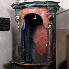 Zdjęcie nr 1: Konfesjonał do słuchania spowiedzi usznej, prostopadłościenny, na podstawie wklęsło-wypukłej, od przodu z drzwiczkami osadzonymi na zawiasach. Ścianki boczne ujęte od frontu pilastrami z podwieszonymi konsolkami, podtrzymującymi wydatny gzyms wyłamany kątowo ponad nimi. Otwór wejściowy poprzedzony wybrzuszającymi się drzwiczkami, zwieńczony lambrekinem. Drzwiczki oraz zaplecek dekorowane płycinami. Całość struktury marmoryzowana w odcieniu granatowym, płyciny czerwone, detal architektoniczny pozłacany.