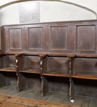 Zdjęcie nr 2: Ława kolatorska, jednorzędowa, ustawiona na niskim prostokątnym podeście, z czterema siedziskami oddzielonymi ściankami o fantazyjnym wykroju. Zaplecek zdobiony nad każdym siedziskiem prostą, prostokątną płyciną w profilowanej ramie. Ława malowana w całości na kolor ciemnobrązowy.