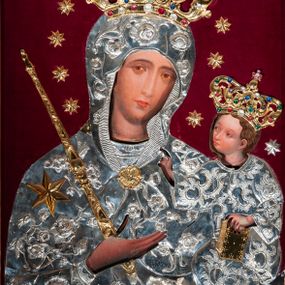 Zdjęcie nr 1: Metalowa sukienka na obraz Matki Boskiej z Dzieciątkiem w ołtarzu głównym, w kształcie obrysu sylwetek Marii i Dzieciątka, z otworami na twarze, dłonie i stopy Jezusa, zdobiona dekoracją roślinną i sześcioramienną złotą gwiazdą umieszczoną na prawym ramieniu Marii. W prawym dolnym narożu fragment sukienki o odmiennej dekoracji (być może pozostałość ze starszej sukienki). Korony w typie zamkniętym, zwieńczone krzyżykami, złocone, kameryzowane. Wokół głowy Matki Boskiej wieniec z gwiazd, w ręku złocone berło. Tło z nowego czerwonego aksamitu.