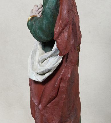 Zdjęcie nr 2: Rzeźba św. Jana Ewangelisty, pełnoplastyczna, z tyłu opracowana, ustawiona na niskim, prostopadłościennym postumencie.  Święty ukazany frontalnie, w nieznacznym kontrapoście, z prawą nogą ugiętą w kolanie, z dłońmi skrzyżowanymi na piersi, z głową przechyloną na prawy bark. Ubrany w długą zieloną suknię z długimi rękawami, ze złotą lamówką na brzegach, oraz czerwony płaszcz z białą podszewką zarzucony na prawe ramię, okrywający plecy i przełożony przez przód figury. Twarz szeroka; lekko rozchylone, wąskie usta; duże i migdałowate oczy. Włosy sięgające do ramion, delikatnie falowane. Szaty silnie drapowane.