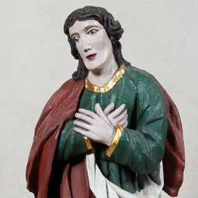 Zdjęcie nr 1: Rzeźba św. Jana Ewangelisty, pełnoplastyczna, z tyłu opracowana, ustawiona na niskim, prostopadłościennym postumencie.  Święty ukazany frontalnie, w nieznacznym kontrapoście, z prawą nogą ugiętą w kolanie, z dłońmi skrzyżowanymi na piersi, z głową przechyloną na prawy bark. Ubrany w długą zieloną suknię z długimi rękawami, ze złotą lamówką na brzegach, oraz czerwony płaszcz z białą podszewką zarzucony na prawe ramię, okrywający plecy i przełożony przez przód figury. Twarz szeroka; lekko rozchylone, wąskie usta; duże i migdałowate oczy. Włosy sięgające do ramion, delikatnie falowane. Szaty silnie drapowane.