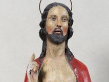 Zdjęcie nr 1: Rzeźba Chrystusa Zmartwychwstałego, pełnoplastyczna, z tyłu opracowana, ustawiona na niskim, okrągłym cokole. Chrystus ukazany w całej postaci, frontalnie, z prawą ręką uniesioną w geście błogosławieństwa, w lewej trzyma chorągiew. Ubrany w czerwony płaszcz z niebieską podszewką, spływający z lewego ramienia, przez przód postaci, na prawe przedramię, tworząc znaczną fałdę misową. Korpus ciała nagi. Twarz podłużna, z lekko rozchylonymi ustami, okolona krótko przystrzyżoną brodą i ciemnobrązowymi włosami opadającymi na plecy. Wokół głowy złoty, kolisty nimb z metalowego pręta. Czerwona chorągiew z tkaniny zawieszona na długim, złotym i drewnianym drzewcu zakończonym krzyżykiem.