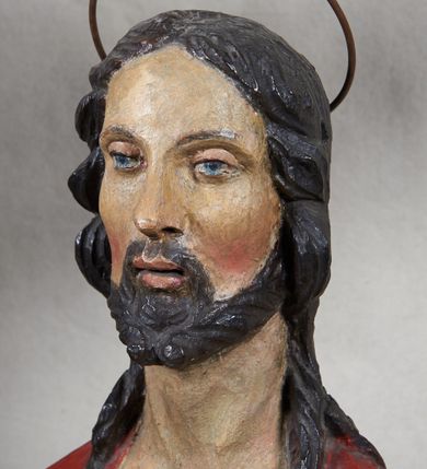 Zdjęcie nr 5: Rzeźba Chrystusa Zmartwychwstałego, pełnoplastyczna, z tyłu opracowana, ustawiona na niskim, okrągłym cokole. Chrystus ukazany w całej postaci, frontalnie, z prawą ręką uniesioną w geście błogosławieństwa, w lewej trzyma chorągiew. Ubrany w czerwony płaszcz z niebieską podszewką, spływający z lewego ramienia, przez przód postaci, na prawe przedramię, tworząc znaczną fałdę misową. Korpus ciała nagi. Twarz podłużna, z lekko rozchylonymi ustami, okolona krótko przystrzyżoną brodą i ciemnobrązowymi włosami opadającymi na plecy. Wokół głowy złoty, kolisty nimb z metalowego pręta. Czerwona chorągiew z tkaniny zawieszona na długim, złotym i drewnianym drzewcu zakończonym krzyżykiem.