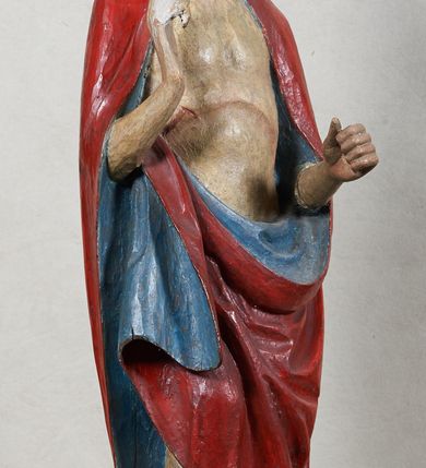 Zdjęcie nr 2: Rzeźba Chrystusa Zmartwychwstałego, pełnoplastyczna, z tyłu opracowana, ustawiona na niskim, okrągłym cokole. Chrystus ukazany w całej postaci, frontalnie, z prawą ręką uniesioną w geście błogosławieństwa, w lewej trzyma chorągiew. Ubrany w czerwony płaszcz z niebieską podszewką, spływający z lewego ramienia, przez przód postaci, na prawe przedramię, tworząc znaczną fałdę misową. Korpus ciała nagi. Twarz podłużna, z lekko rozchylonymi ustami, okolona krótko przystrzyżoną brodą i ciemnobrązowymi włosami opadającymi na plecy. Wokół głowy złoty, kolisty nimb z metalowego pręta. Czerwona chorągiew z tkaniny zawieszona na długim, złotym i drewnianym drzewcu zakończonym krzyżykiem.