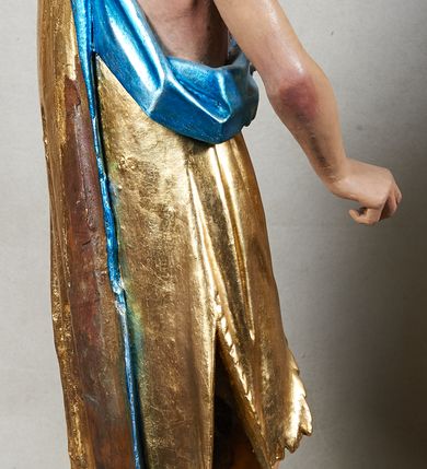 Zdjęcie nr 2: Rzeźba pełnoplastyczna z przedstawieniem Jana Chrzciciela. Święty ukazany frontalnie, w delikatnym kontrapoście, z prawą nogą ugiętą w kolanie, ręce ugięte w łokciach, lewą dłonią podtrzymuje przed sobą księgę, prawa ułożona w geście trzymania niezachowanego atrybutu. Ubrany w krótką szatę (zapewne ze skóry wielbłąda), sięgającą do kolan i odsłaniającą prawe ramię, oraz złoty płaszcz z niebieską podszewką, zarzucony na lewe ramię. Twarz podłużna, okolona ciemną brodą i silnie falowanymi włosami, sięgającymi do ramion i opadającymi na plecy. Karnacja jasna, policzki silnie zarumienione.