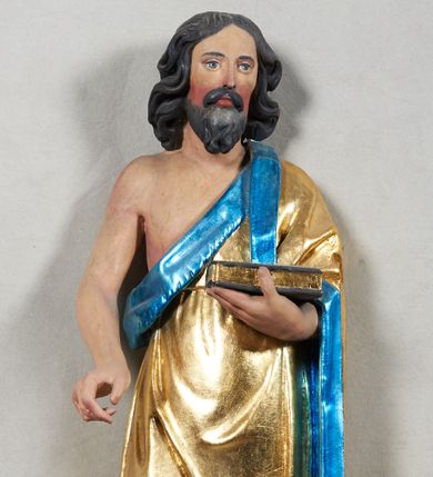 Zdjęcie nr 1: Rzeźba pełnoplastyczna z przedstawieniem Jana Chrzciciela. Święty ukazany frontalnie, w delikatnym kontrapoście, z prawą nogą ugiętą w kolanie, ręce ugięte w łokciach, lewą dłonią podtrzymuje przed sobą księgę, prawa ułożona w geście trzymania niezachowanego atrybutu. Ubrany w krótką szatę (zapewne ze skóry wielbłąda), sięgającą do kolan i odsłaniającą prawe ramię, oraz złoty płaszcz z niebieską podszewką, zarzucony na lewe ramię. Twarz podłużna, okolona ciemną brodą i silnie falowanymi włosami, sięgającymi do ramion i opadającymi na plecy. Karnacja jasna, policzki silnie zarumienione.