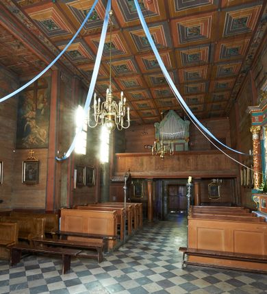 Zdjęcie nr 28: Prezbiterium. Strop pokryty dekoracją malarską imitującą kasetony wypełnione rozetami oraz umieszczonymi pomiędzy nimi krzyżami wypełnionymi liśćmi na ramionach i rozetami na skrzyżowaniu. Na ścianach bocznych prezbiterium, w arkadach podtrzymywanych przez kolumny popiersia apostołów oraz popiersia mężczyzn w strojach szlacheckich ukazane na tle zielonych obić (genealogia Chrystusa). Pod nimi fryz z łacińskimi napisami od dołu zdobiony girlandami z uskrzydlonymi główkami anielskimi oraz puklowanymi wazami. Na ścianach również herby: m.in. Łabędź, Jastrzębiec.  Nawa główna. Strop pokryty dekoracją malarską imitującą kasetony z rozetami. Na ścianach bocznych nawy głównej: na ścianie północnej cykl pasyjny w kwadratowych obramieniach z przedstawieniami: Modlitwa w Ogrojcu, Biczowanie Chrystusa, Chrystus Umęczony, Ecce Homo, Upadek pod krzyżem oraz słabo czytelny cykl maryjny z przedstawieniami: Zwiastowanie, Boże Narodzenie, Hołd Trzech Króli oraz Ucieczka do Egiptu i Rzeź niewiniątek, Jezus nauczający w świątyni. Na ścianie południowej nawy w arkadach umieszczono przedstawienia św. Wojciecha z wiosłem i św. Stanisława z Piotrowinem. Na balustradzie chóru muzycznego zachowały się częściowo trzy sceny ilustrujące przypowieść o bogaczu i Łazarzu oraz data: 1562. Kolorystyka pastelowa z przewagą zieleni, beżu i czerwieni z mocno zaznaczonymi konturami.