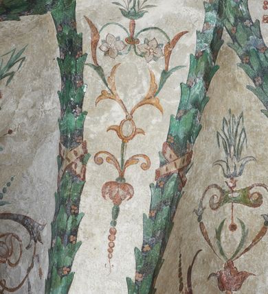 Zdjęcie nr 3: Strukturę architektoniczną kaplicy, wzniesionej na rzucie kwadratu ze ściętymi od północy narożami i sklepionej krzyżowo z lunetami spływającymi na wsporniki w kształcie kapiteli jońskich, podkreśla ornament złożony z motywów roślinnych. Szwy sklepienne pokrywa wić z liści i owoców wawrzynu miejscami przewiązana skrzyżowaną wstęgą. Pola sklepienia wypełniają medaliony z przedstawieniami czterech ewangelistów w ramach zdobionych ornamentem okuciowym, dzbany z kwiatami lilii, z uszami o motywach antropomorficznych oraz wici roślinne m. in. z motywami kwiatów lilii, falującymi wstęgami, zwisami z owoców oraz z tkaninami. Na ścianach sceny: Św. Stanisław wskrzeszający Piotrowina, Św. Wojciech, Przemienienie Pańskie na górze Tabor oraz kartusze herbowe. Kolorystyka pastelowa z przewagą zieleni, czerwieni i beżu.