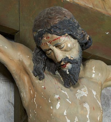 Zdjęcie nr 16: W centrum krzyż z figurą Chrystusa umarłego. Postać w lekkim zwisie o szeroko rozłożonych ramionach, głowa opada na prawe ramie. Twarz szczupła, wyraźnie rzeźbiona, okolona krótką brodą; oczy zamknięte, długi nos, usta delikatnie rozchylone. Włosy w postaci delikatnych loków opadają na ramię i plecy. Ciało szczupłe, ascetyczne, o plastycznie kształtowanej anatomii, z zaznaczonymi śladami męki. Nogi ugięte w kolanach, stopy przebite jednym gwoździem, założone prawa na lewą. Perizonium przewiązane podwójnym sznurem, odsłaniające prawe biodro, ze zwisem na prawym boku. Po prawej stronie krzyża figura Matki Boskiej, zwrócona en face, w kontrapoście; dłonie splecione, wyciągnięte przed siebie. Twarz okrągła o wyraźnych liniach łuków brwiowych i nosa, półprzymkniętych oczach. Ubrana w różową suknię przewiązaną w talii oraz granatowy płaszcz podbity czerwoną podszewką, zarzucony diagonalnie na lewe ramię i opadający na prawą nogę. Na głowie biały welon. Po lewej stronie krzyża figura św. Jana, zwrócona en face, w kontrapoście, o esowato wygiętej sylwetce; prawą rękę trzyma na piersi, lewa pozostaje opuszczona wzdłuż ciała. Twarz pełna, młodzieńcza, podkreślone linie łuków brwiowych i nosa. Włosy długie, falowane, opadają na ramiona. Ubrany w zieloną tunikę oraz czerwony płaszcz przerzucony diagonalnie przez prawy bok, przewiązane w talii. Polichromia naturalistyczna, perizonium złocone.Grupa na tle malowanego miasta oraz skłębionego szaroróżowego nieba.