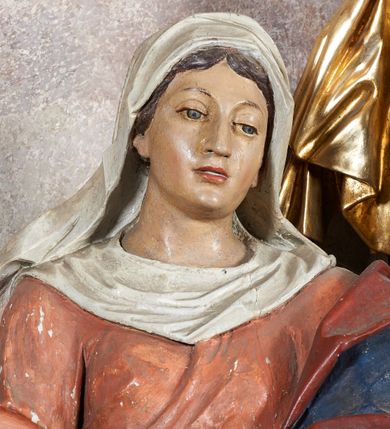 Zdjęcie nr 5: W centrum krzyż z figurą Chrystusa umarłego. Postać w lekkim zwisie o szeroko rozłożonych ramionach, głowa opada na prawe ramie. Twarz szczupła, wyraźnie rzeźbiona, okolona krótką brodą; oczy zamknięte, długi nos, usta delikatnie rozchylone. Włosy w postaci delikatnych loków opadają na ramię i plecy. Ciało szczupłe, ascetyczne, o plastycznie kształtowanej anatomii, z zaznaczonymi śladami męki. Nogi ugięte w kolanach, stopy przebite jednym gwoździem, założone prawa na lewą. Perizonium przewiązane podwójnym sznurem, odsłaniające prawe biodro, ze zwisem na prawym boku. Po prawej stronie krzyża figura Matki Boskiej, zwrócona en face, w kontrapoście; dłonie splecione, wyciągnięte przed siebie. Twarz okrągła o wyraźnych liniach łuków brwiowych i nosa, półprzymkniętych oczach. Ubrana w różową suknię przewiązaną w talii oraz granatowy płaszcz podbity czerwoną podszewką, zarzucony diagonalnie na lewe ramię i opadający na prawą nogę. Na głowie biały welon. Po lewej stronie krzyża figura św. Jana, zwrócona en face, w kontrapoście, o esowato wygiętej sylwetce; prawą rękę trzyma na piersi, lewa pozostaje opuszczona wzdłuż ciała. Twarz pełna, młodzieńcza, podkreślone linie łuków brwiowych i nosa. Włosy długie, falowane, opadają na ramiona. Ubrany w zieloną tunikę oraz czerwony płaszcz przerzucony diagonalnie przez prawy bok, przewiązane w talii. Polichromia naturalistyczna, perizonium złocone.Grupa na tle malowanego miasta oraz skłębionego szaroróżowego nieba.